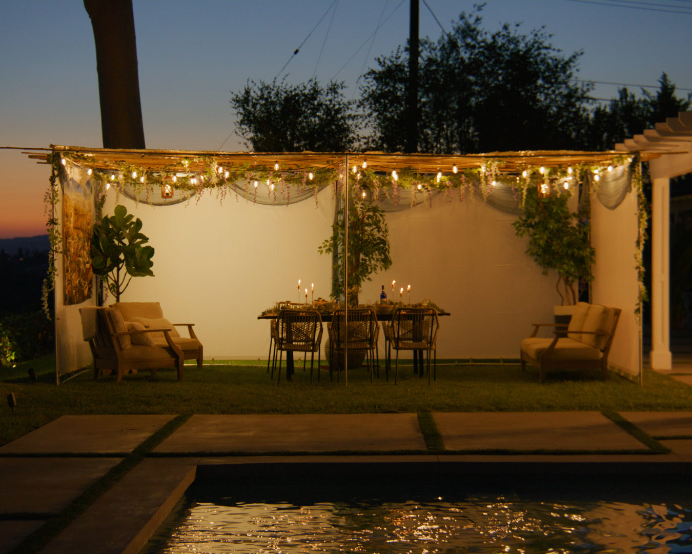 Expandable Sieger Sukkah kit with kosher bamboo Schach mats and Sukkah lighting at night, with a set table and chairs